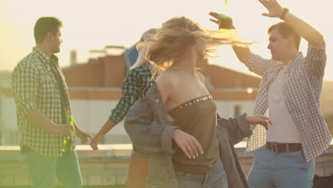 The-young-American-girl-is-dancing-on-the-roof-with-her-five-friends-on-the-party.-She-smiles-and-enjoys-the-time-in-shorts-and-a-light-denim-jacket-during-summer-evening.